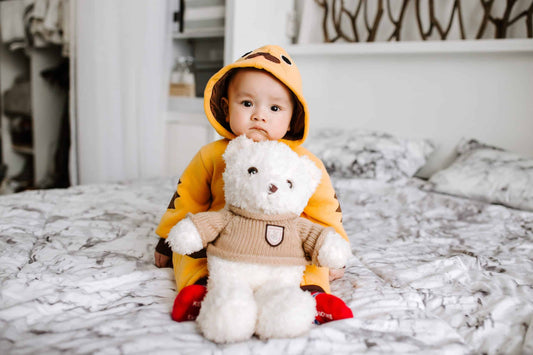 Child in raincoat sitting on bed holding teddy bear