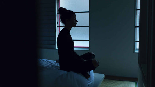 image of woman sitting up in bed at night unable to sleep in the dark next to window