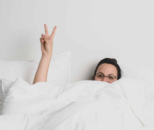 image of woman in bed with white sheets and throwing a peace sign