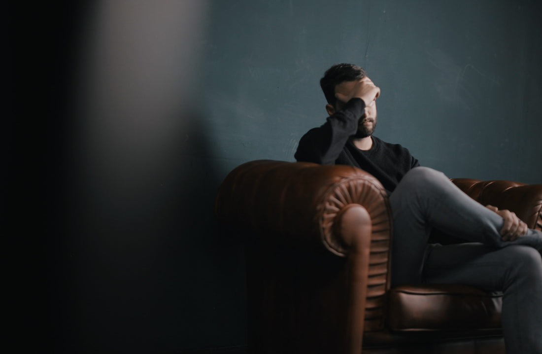 Image of man on a leather chair holding his hand over his brow